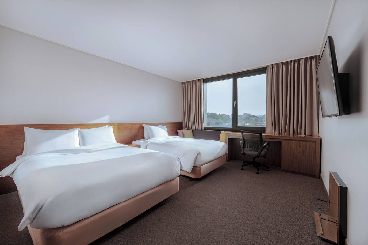 A hotel room with two beds, a desk, a chair, and a TV mounted on the wall.