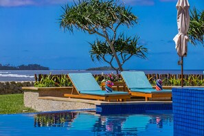 Ein Poolbereich mit zwei Liegestühlen, einem Baum und Blick aufs Meer.