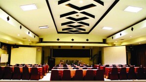 Uma sala de conferência com palco, diversas mesas e cadeiras dispostas para uma reunião.