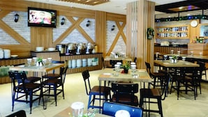 Restaurante com várias mesas e cadeiras, um espaço de bar e uma televisão na parede.