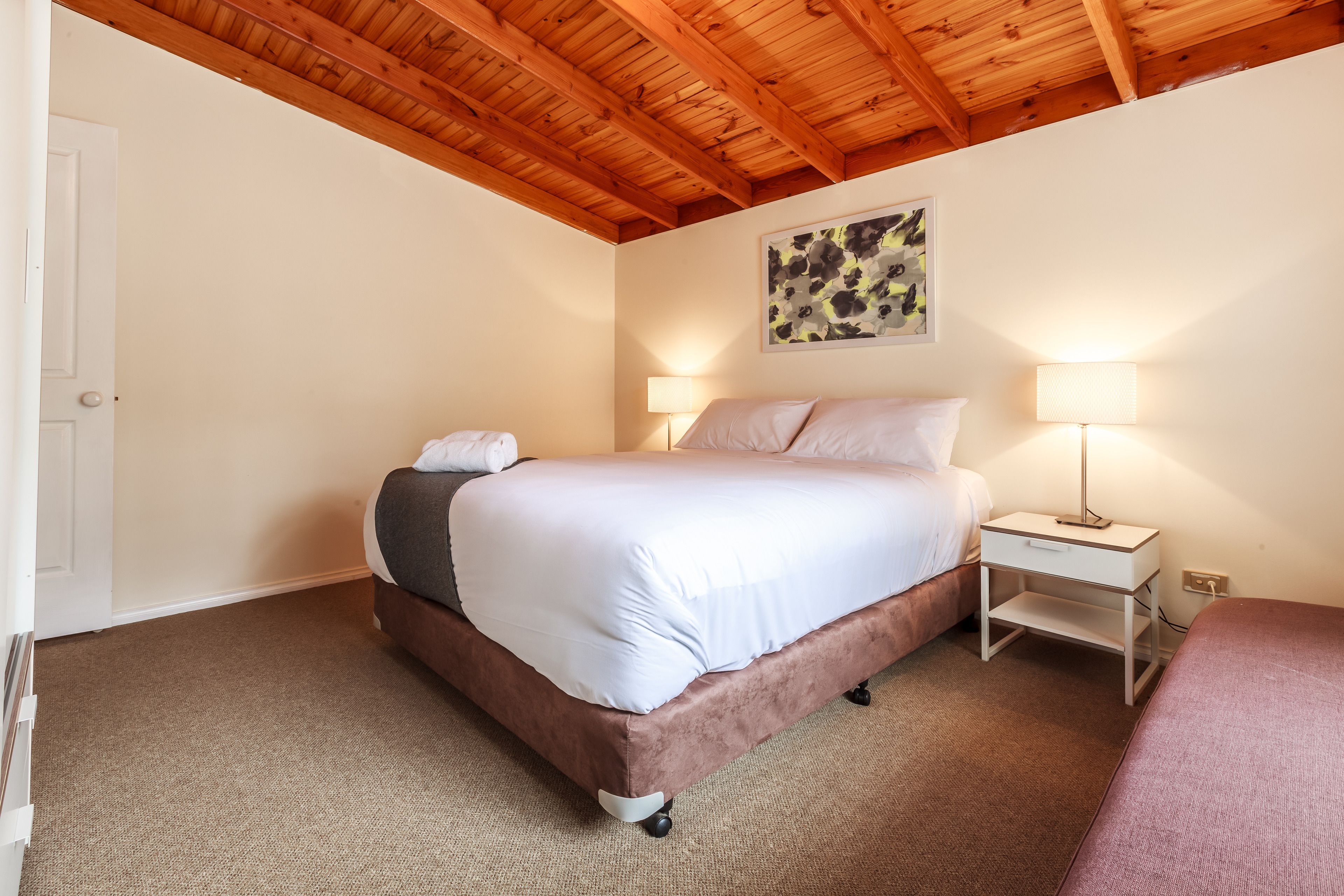 A bedroom with a bed, bedside tables, and a ceiling with wooden beams.