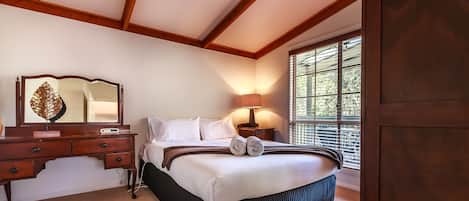 A bedroom with a large bed, a wooden dresser, a mirror, and a window with blinds.