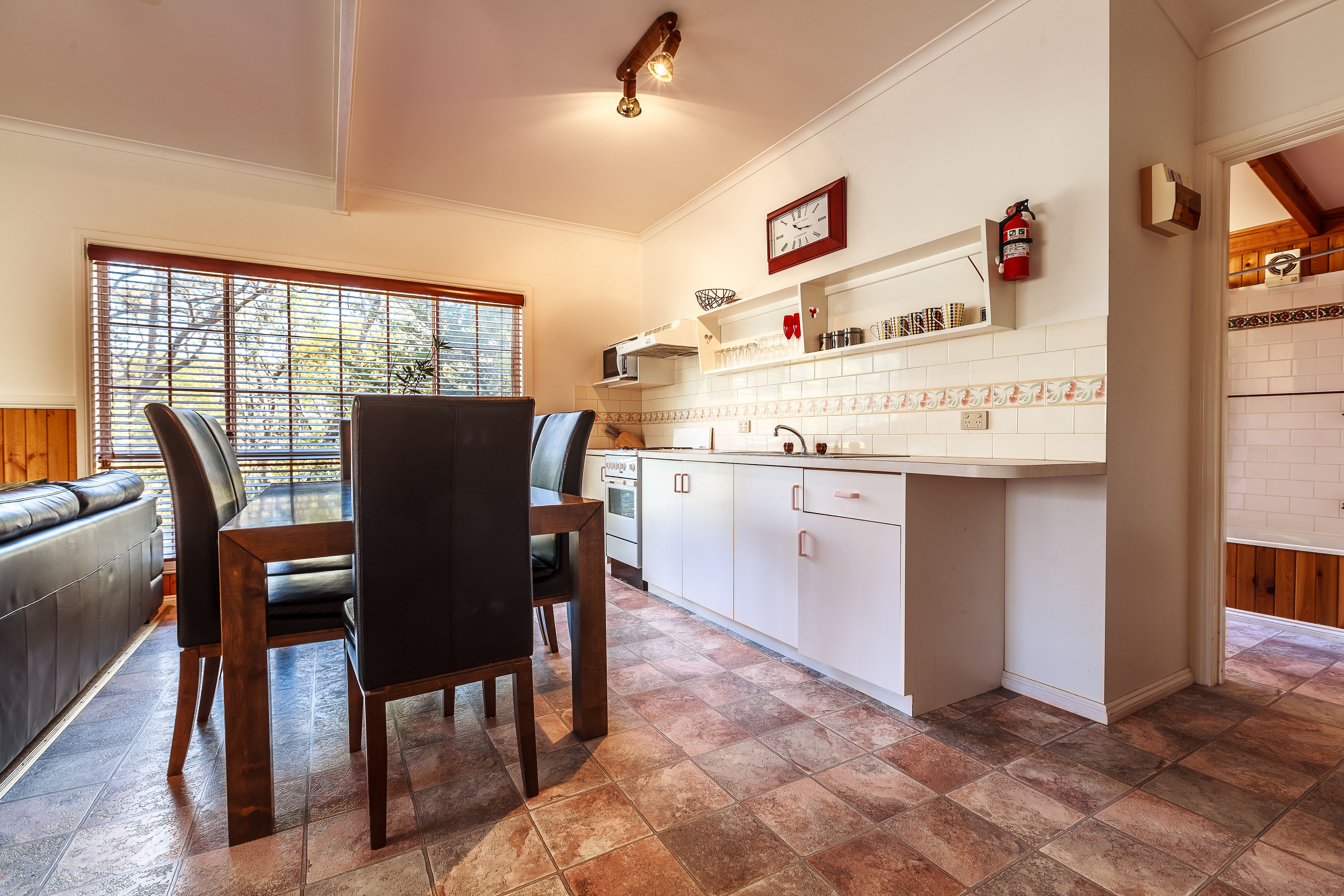 A kitchen with white cabinets, a dining table with chairs, and a window with blinds.