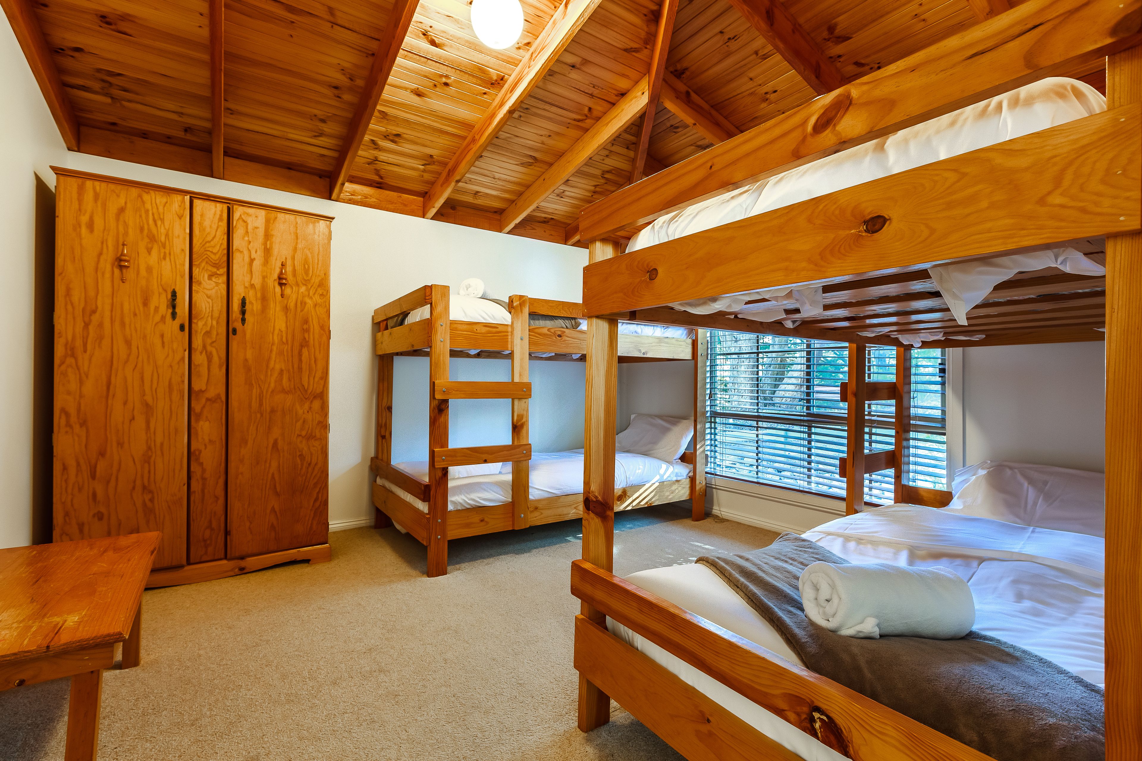 A wooden bunk bed room with a wooden wardrobe and a bench.