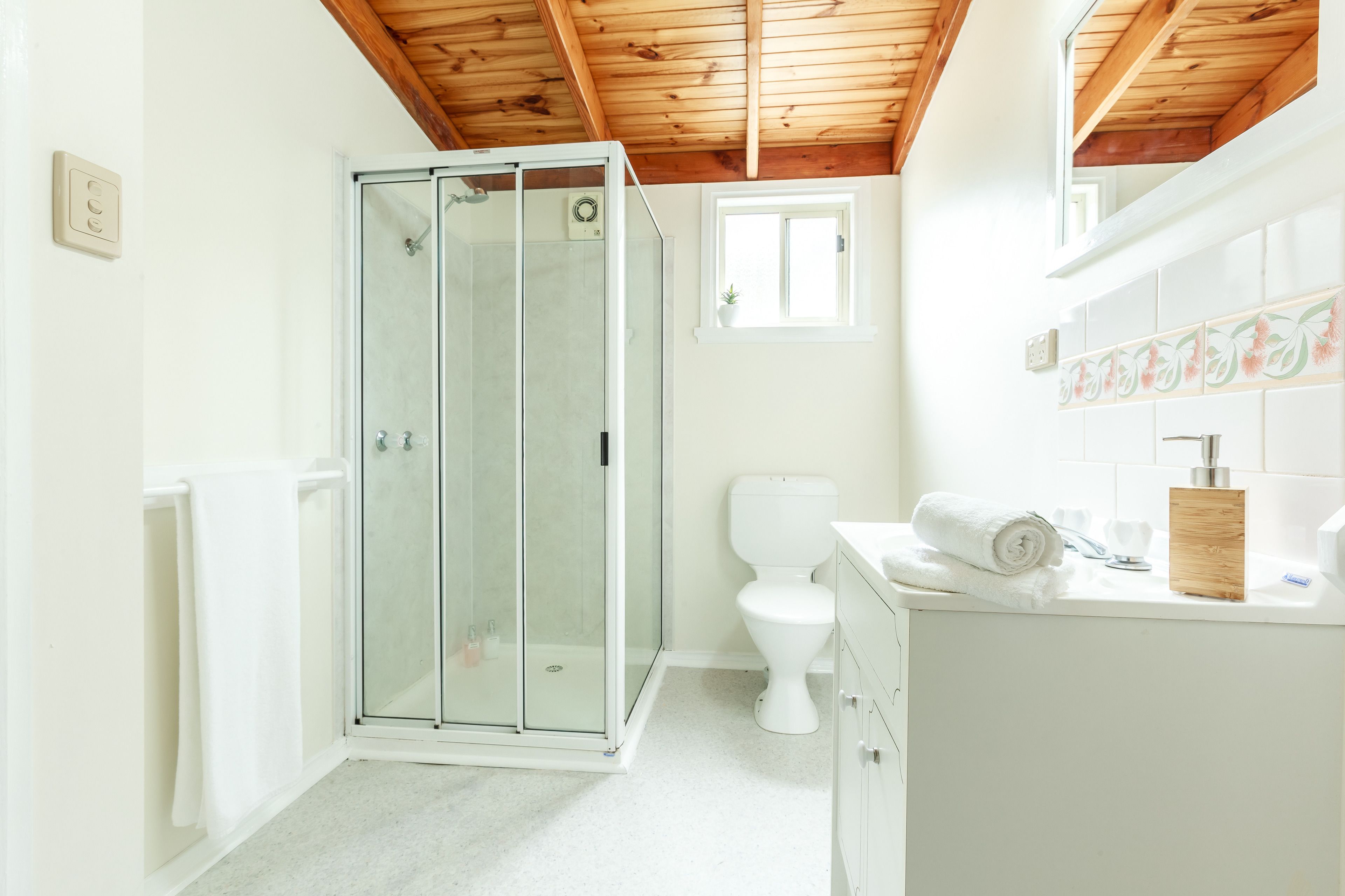 A bathroom with a glass shower enclosure, a toilet, and a sink with a wooden soap holder.