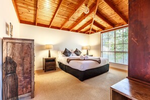 Un dormitorio con techo de madera, un ventanal grande, una cama con almohadas, una mesita de noche y un aparador.