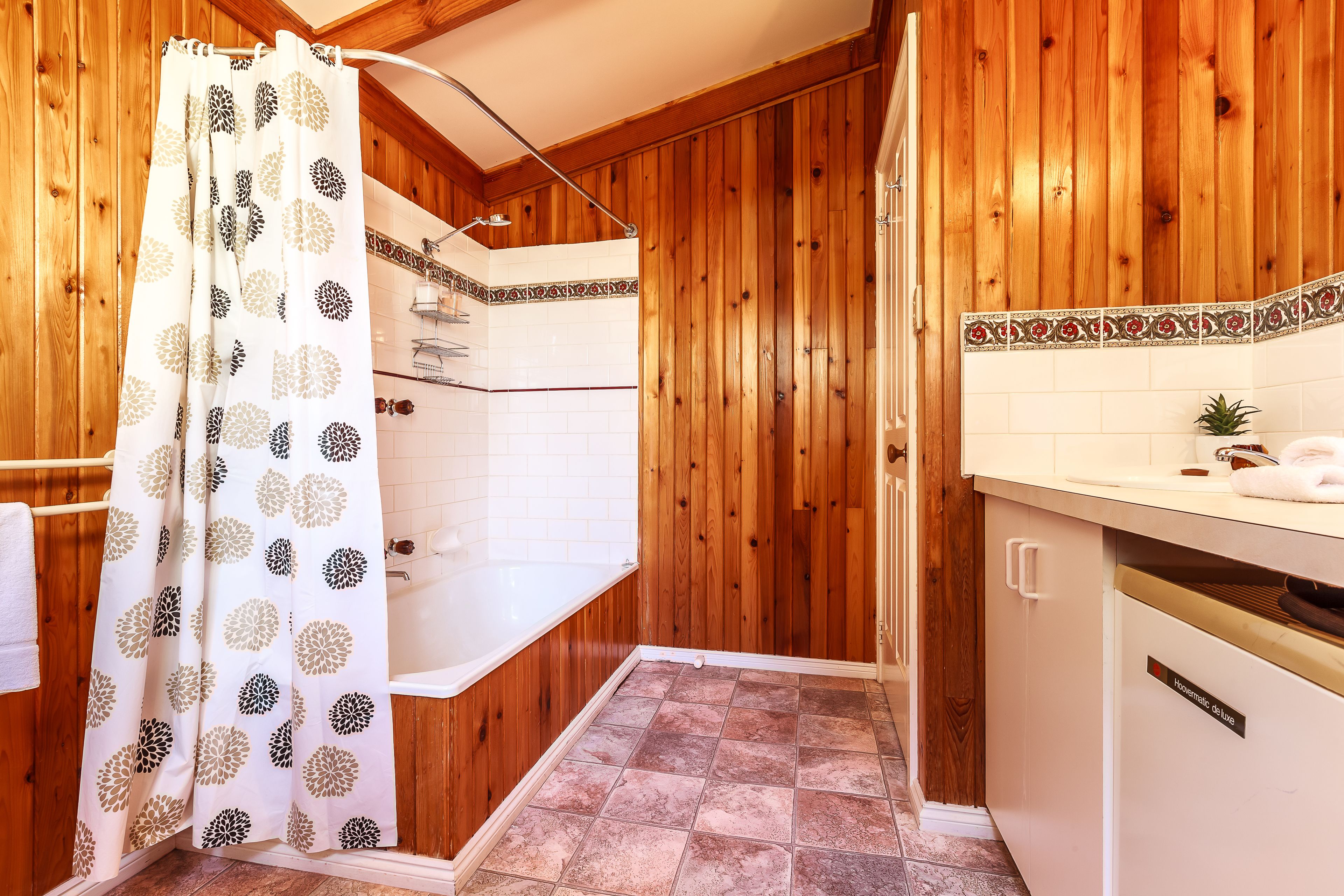 Een badkamer met houten wanden, een douche en een wit wastafelmeubel.