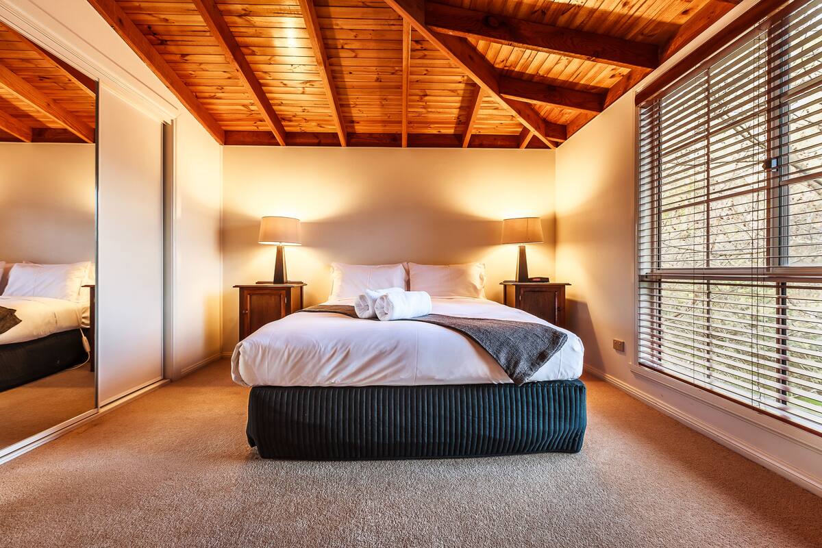 Ein Schlafzimmer mit Holzboden, einem großen Bett mit weißen Leinen, zwei Nachttischen mit Lampen und einem Fenster mit Jalousien.