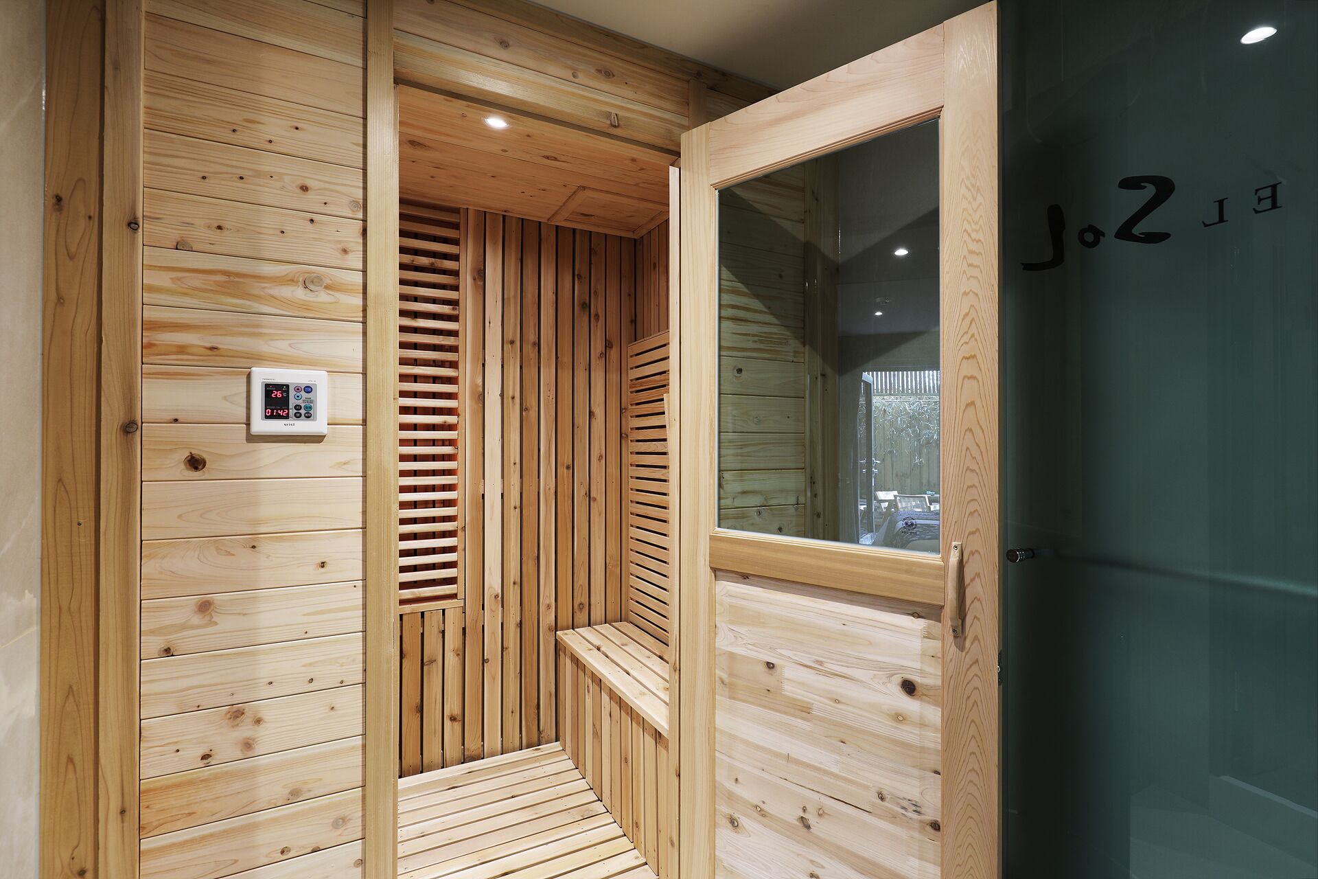 A wooden sauna with a control panel, a bench, and a glass door.