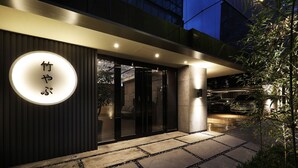 A modern building entrance with a circular illuminated sign, a stone pathway, and a car parking area. - Hotel SoL (Jeonju)