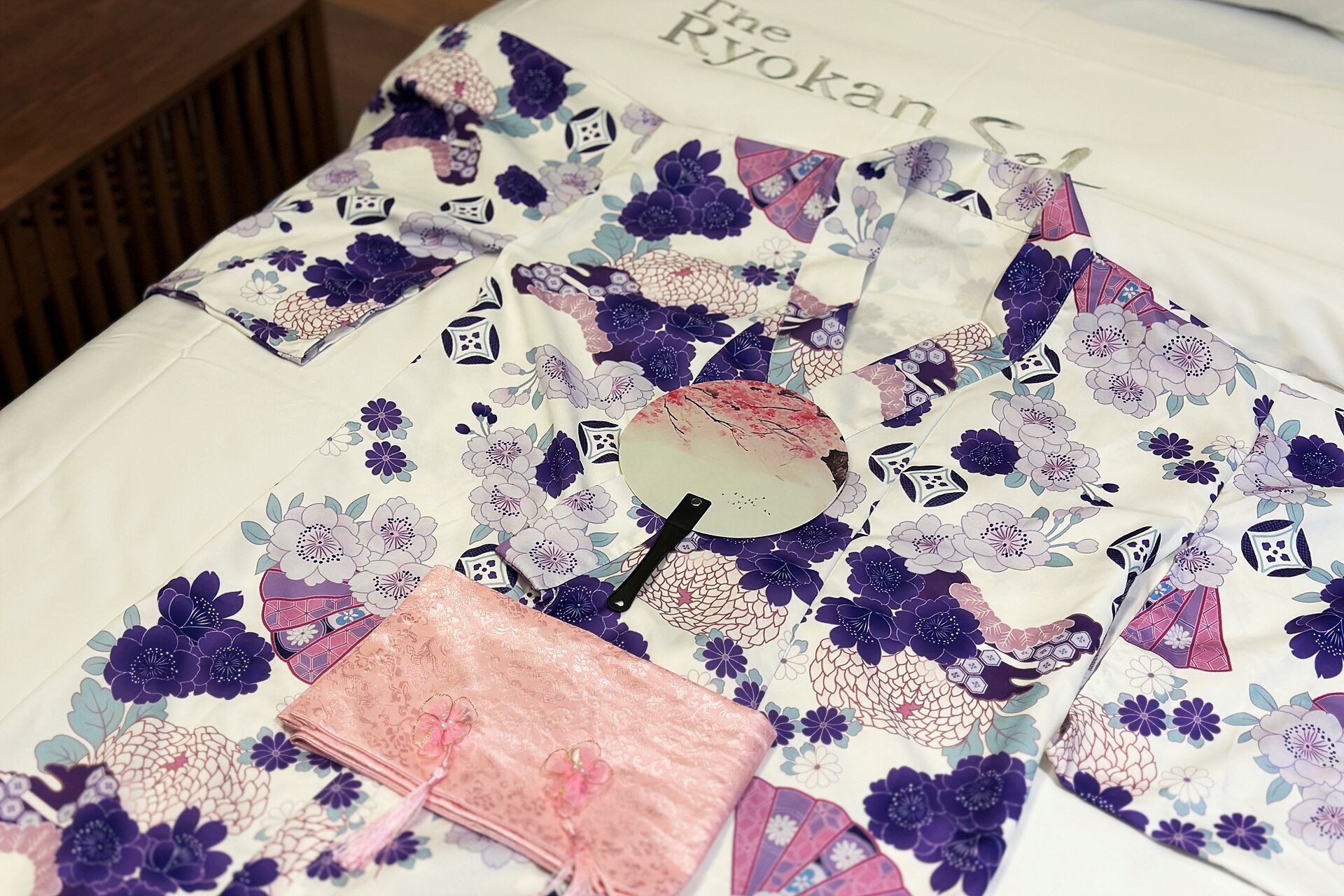 A bed with a floral patterned bedspread and a pink decorative item on it.