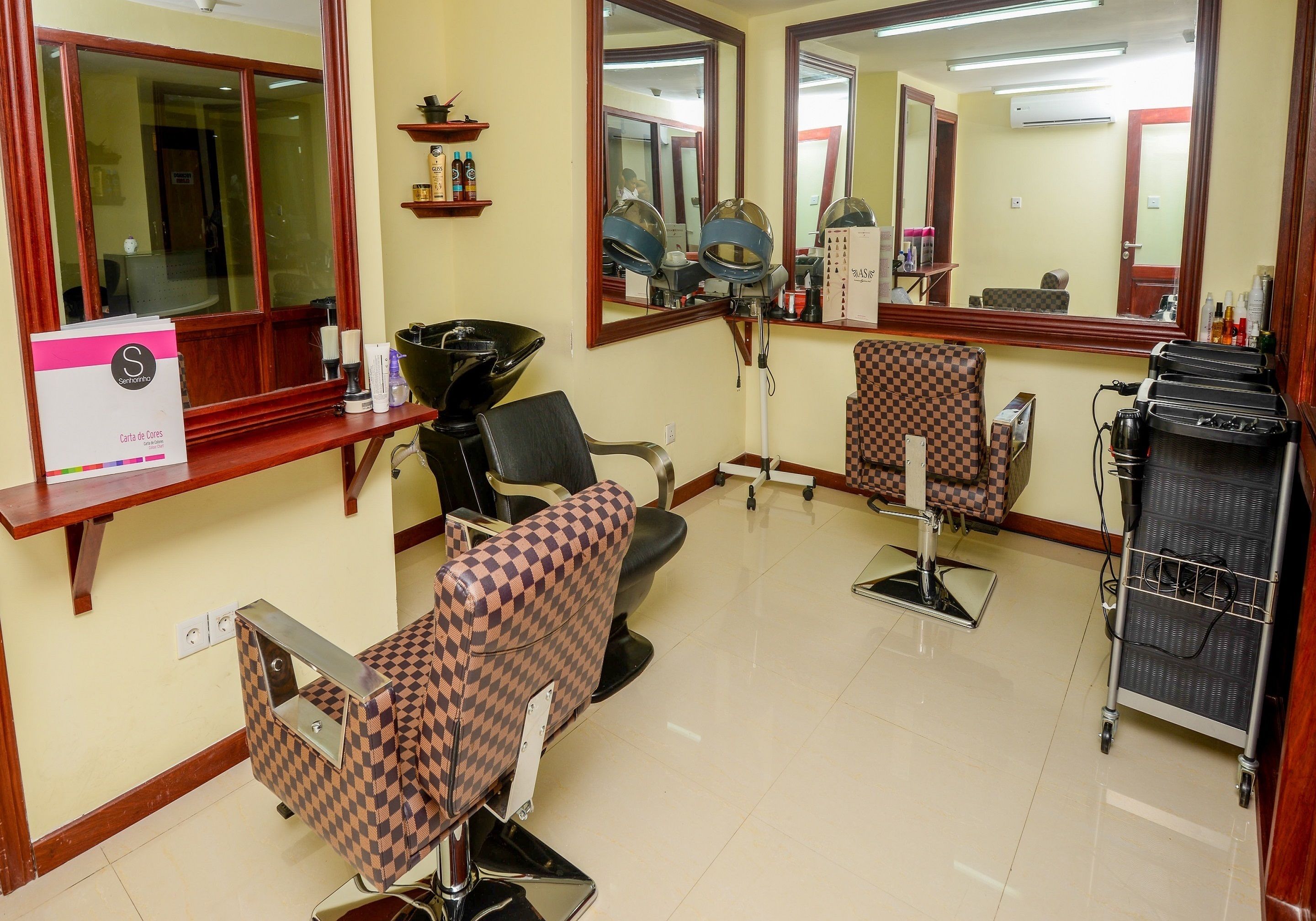 A salon with two checkered chairs, a mirror, and a hairdryer on a cart.