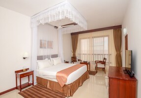 Habitación de hotel con una cama grande, un escritorio, una silla, un televisor y una ventana con cortinas.