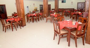 A spacious dining area with multiple tables and chairs, wooden furniture, and a tiled floor. - Raphael's Hotel (Pemba)