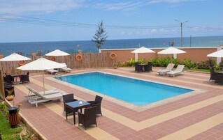 Una piscina con sillas de descanso y sombrillas, rodeada por una valla de madera y vista al mar.