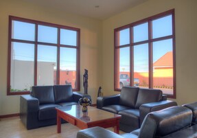 Una sala de estar con un sofá modular, una mesa de centro y ventanas amplias con vistas a un edificio y un coche.