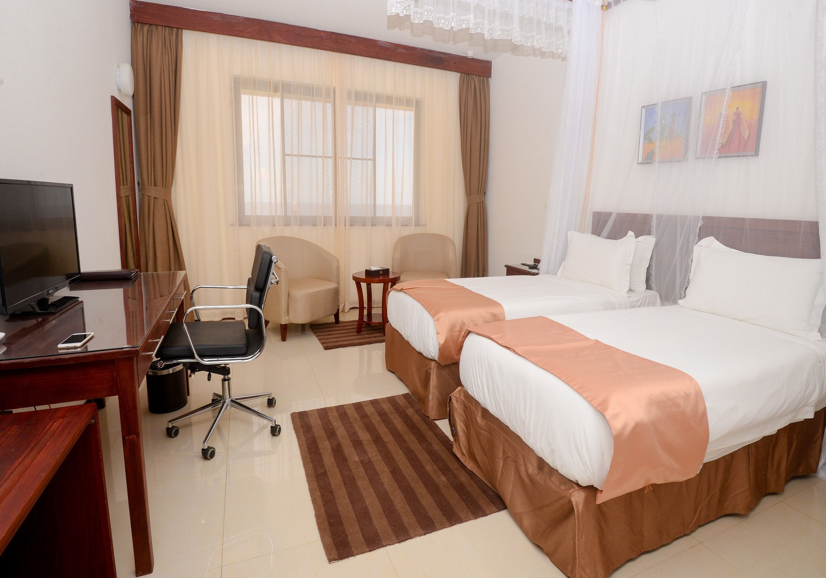 Habitación de hotel con dos camas, un escritorio con computadora, una silla y un televisor.