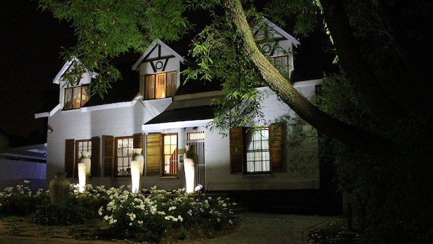 A two-story house with a sloped roof, large windows, and a well-maintained garden with white flowers.