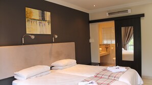 A hotel room with two beds, a painting on the wall, and a bathroom visible through an open door.