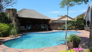 A swimming pool with a thatched-roof structure and a brick wall.