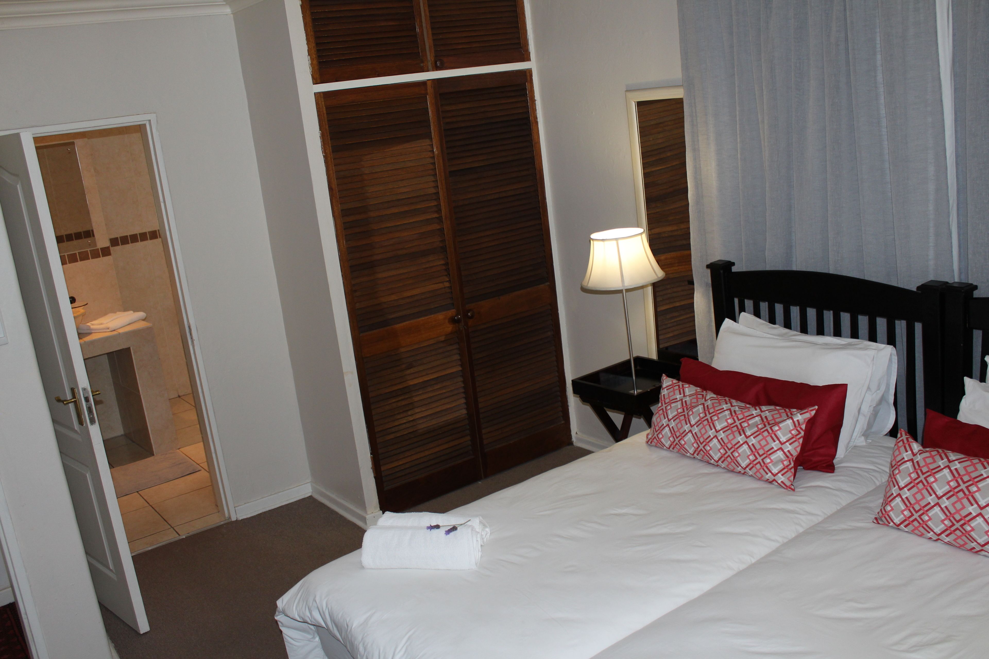 A hotel room with a bed, a nightstand with a lamp, a wooden wardrobe, and a bathroom visible through an open door.