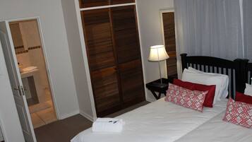 A hotel room with a bed, a nightstand with a lamp, a wooden wardrobe, and a bathroom visible through an open door.