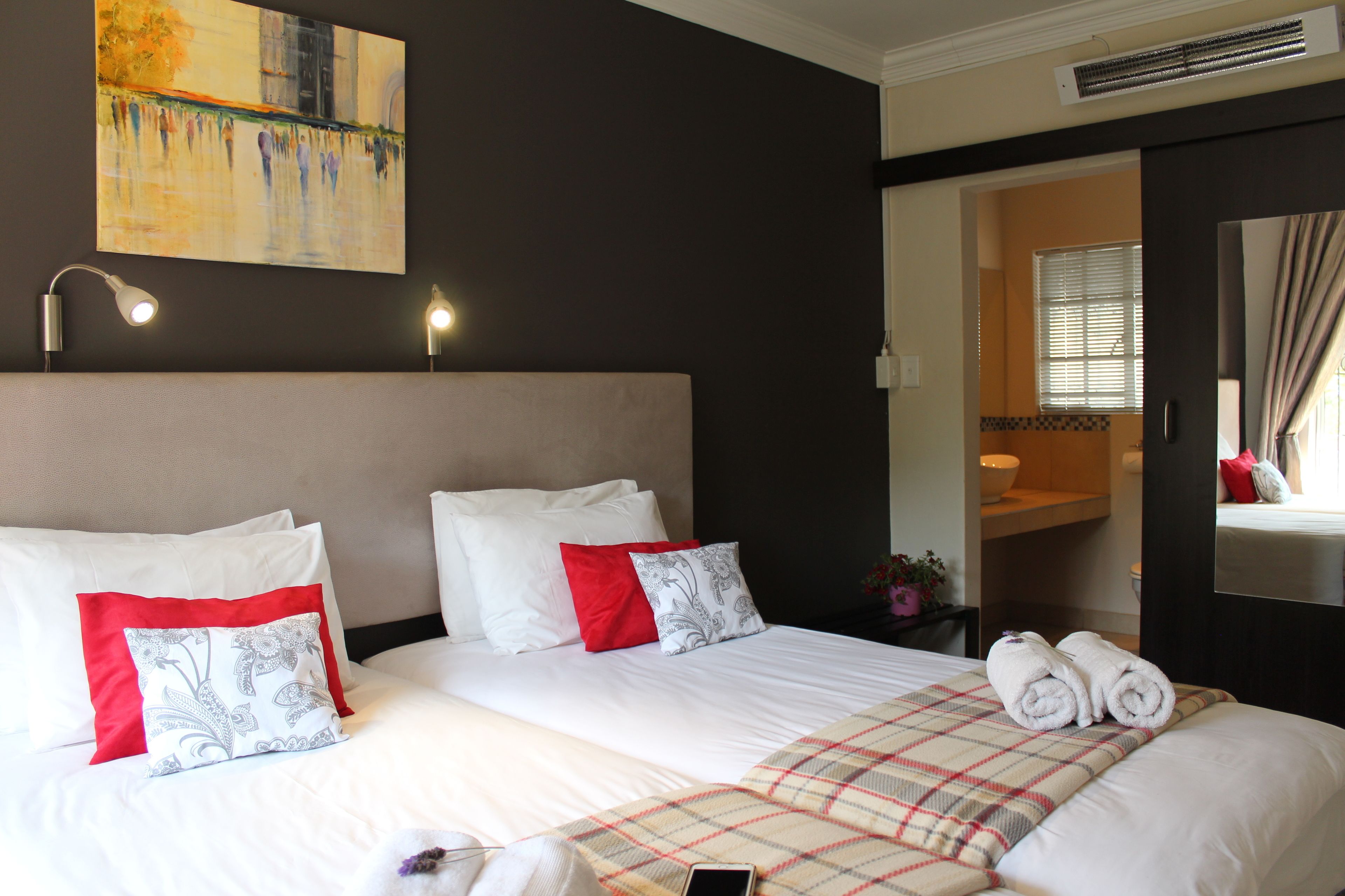 A hotel room with a large bed, a painting on the wall, a bedside table with a lamp, and a bathroom visible through an open door.