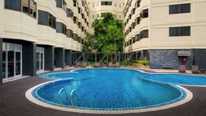 A swimming pool with a tiled edge, surrounded by a wooden deck, and a building with multiple balconies in the background. - Star Convention Hotel (Rayong)