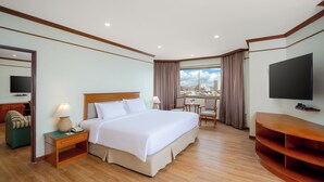 A hotel room with a large bed, a desk with a chair, a television, and a city view. - Star Convention Hotel (Rayong)
