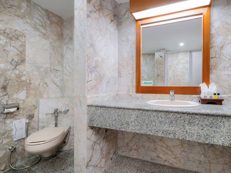 Ein Badezimmer mit Marmorwand, Toilette, Waschbecken mit Spiegel und Duschbereich.
