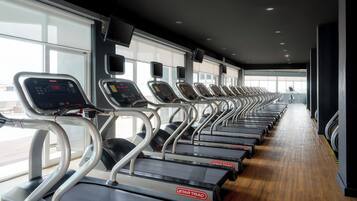 Una fila de cintas de correr StarTrac en un gimnasio con ventanas grandes y suelo de madera.