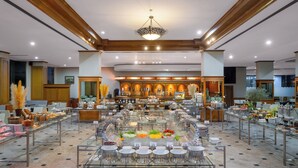 A spacious buffet area with a central glass table surrounded by chairs, and a variety of food and drink options. - Star Convention Hotel (Rayong)