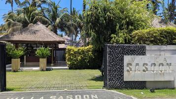 A villa entrance with a thatched roof, a stone wall, and a sign reading 'Villa Sasoon Bali'.