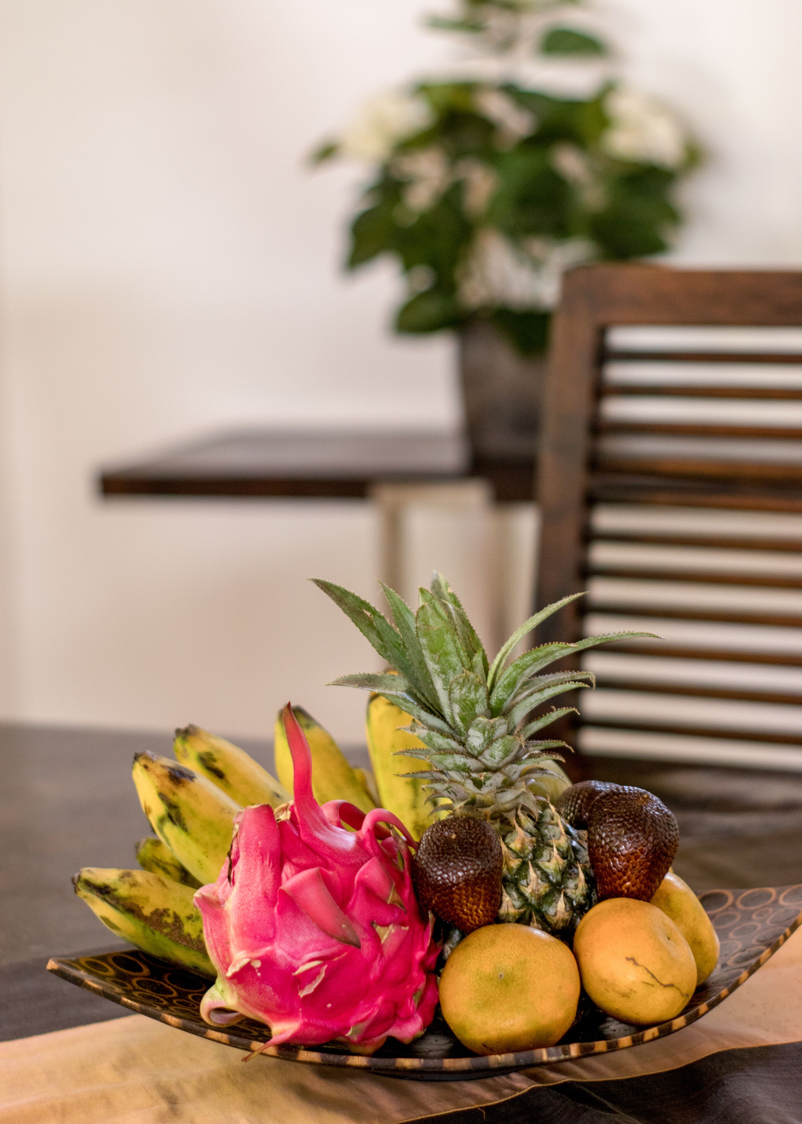 A fruit bowl on a table with a chair in the background.