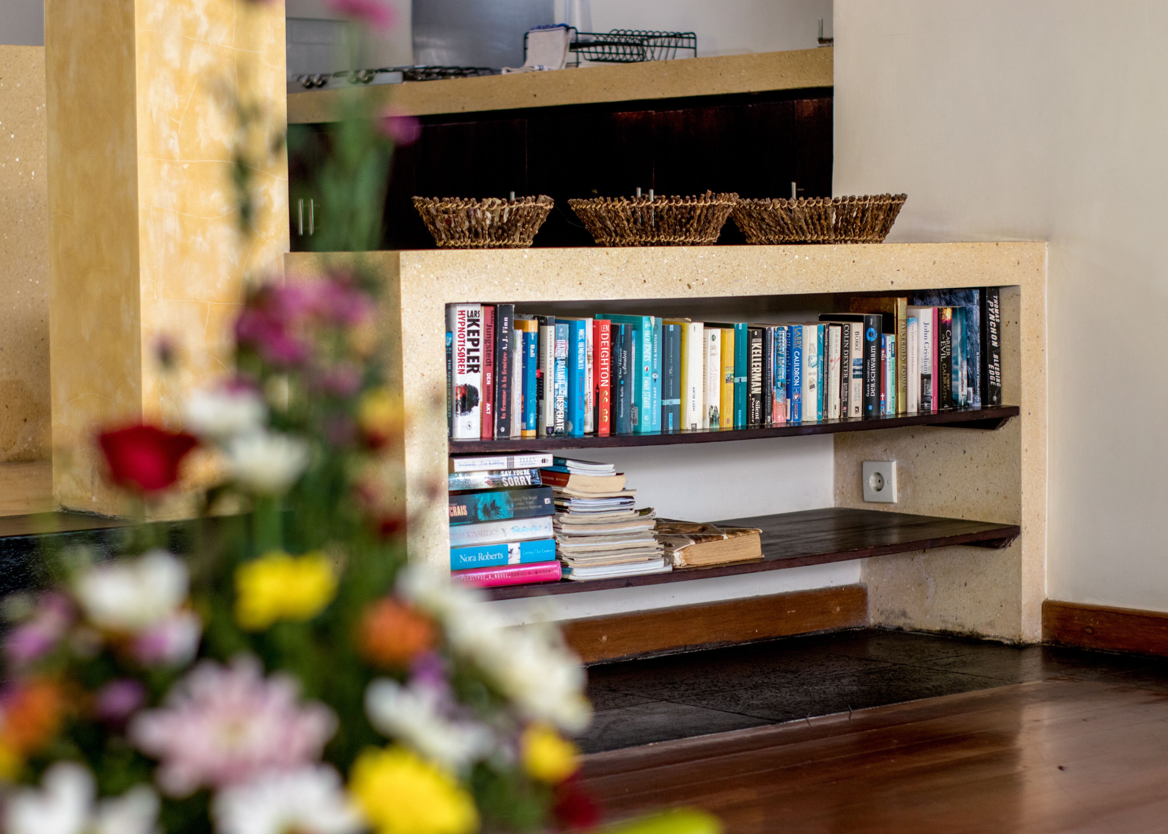 Una estantería llena de libros, suelo de madera y una cesta en el estante.