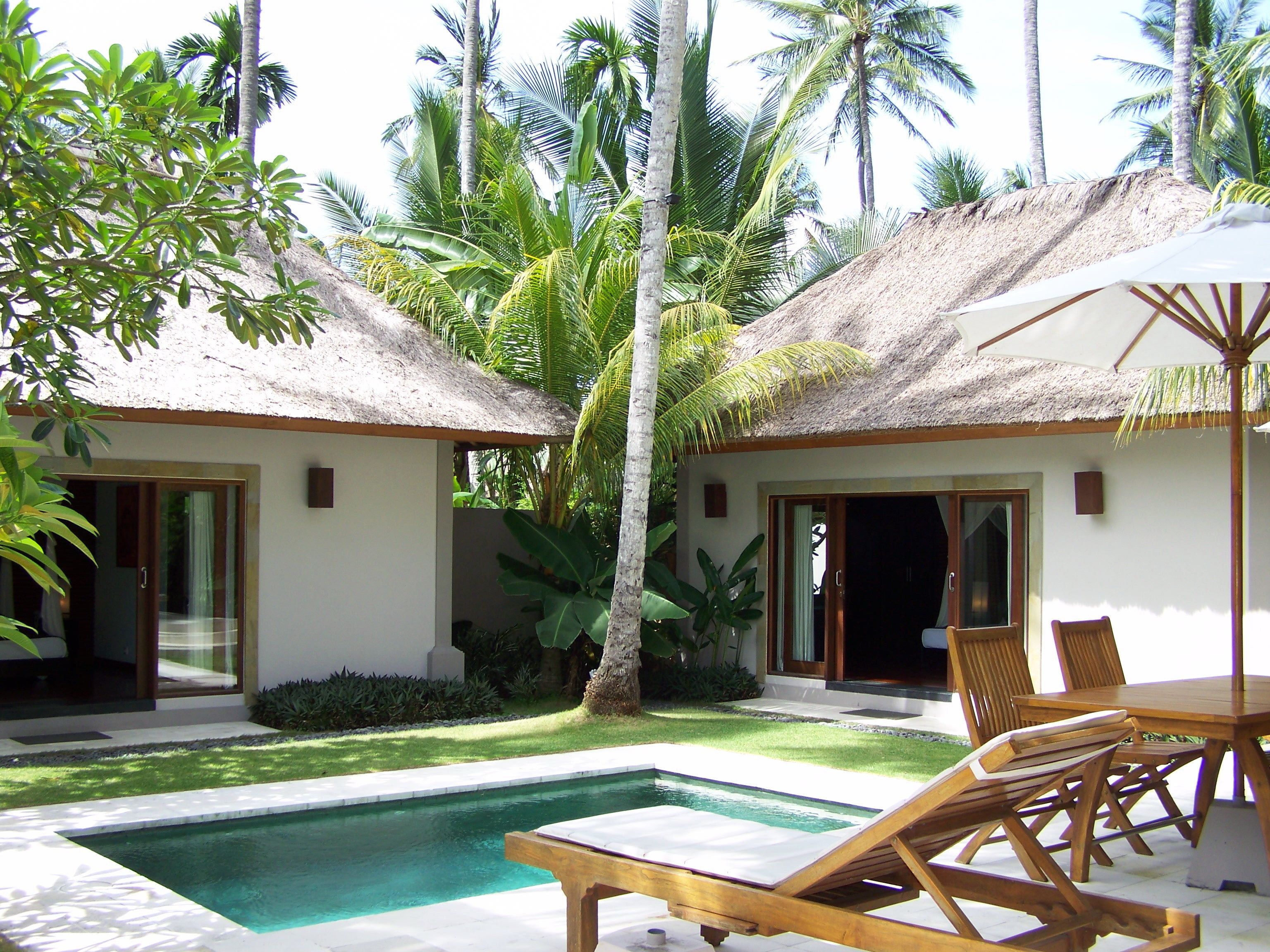 A poolside area with a thatched-roof structure, lounge chairs, and a table.