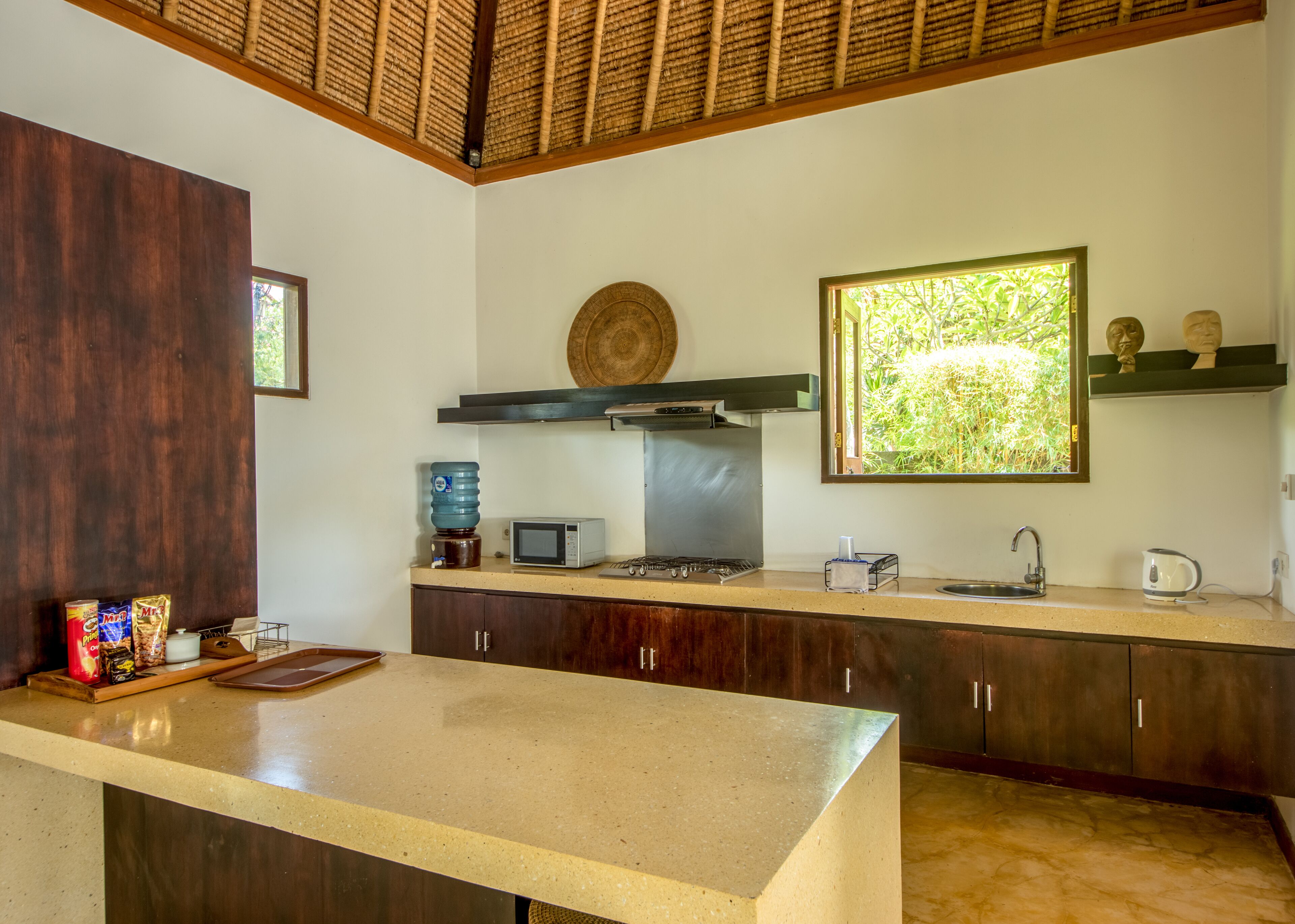 Una cocina con una isla grande, un microondas, un dispensador de agua y un ventanal con vistas a zonas verdes.