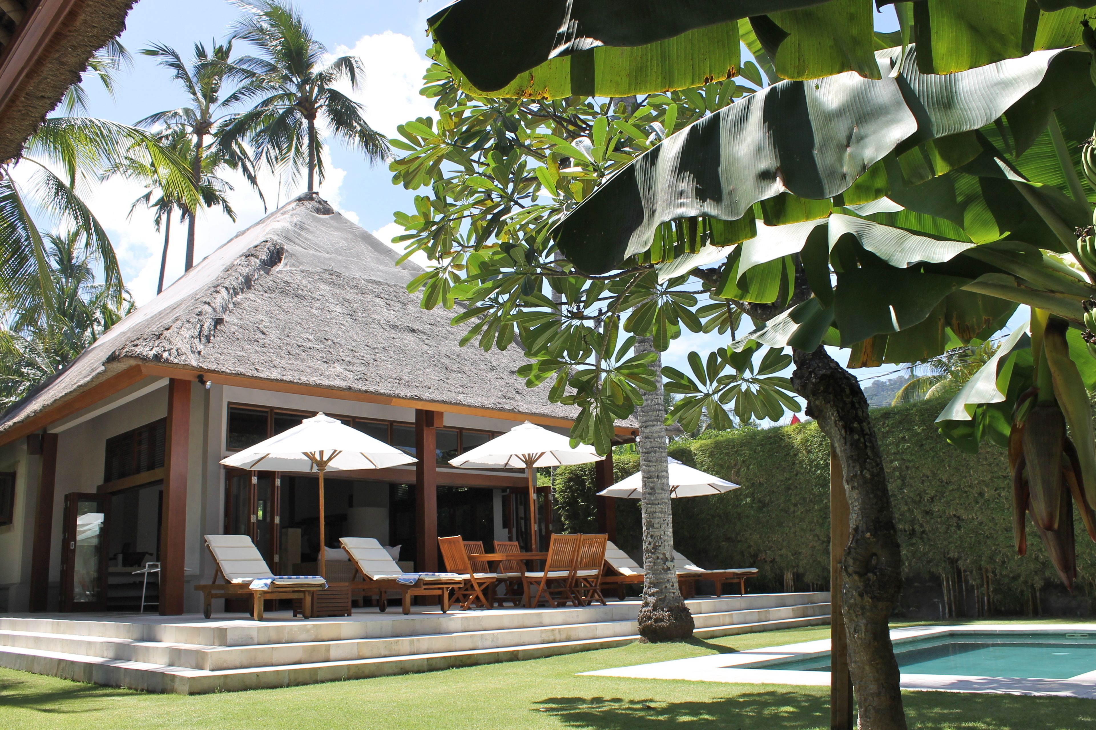 A resort with a thatched-roof building, outdoor seating area with umbrellas, and a pool.