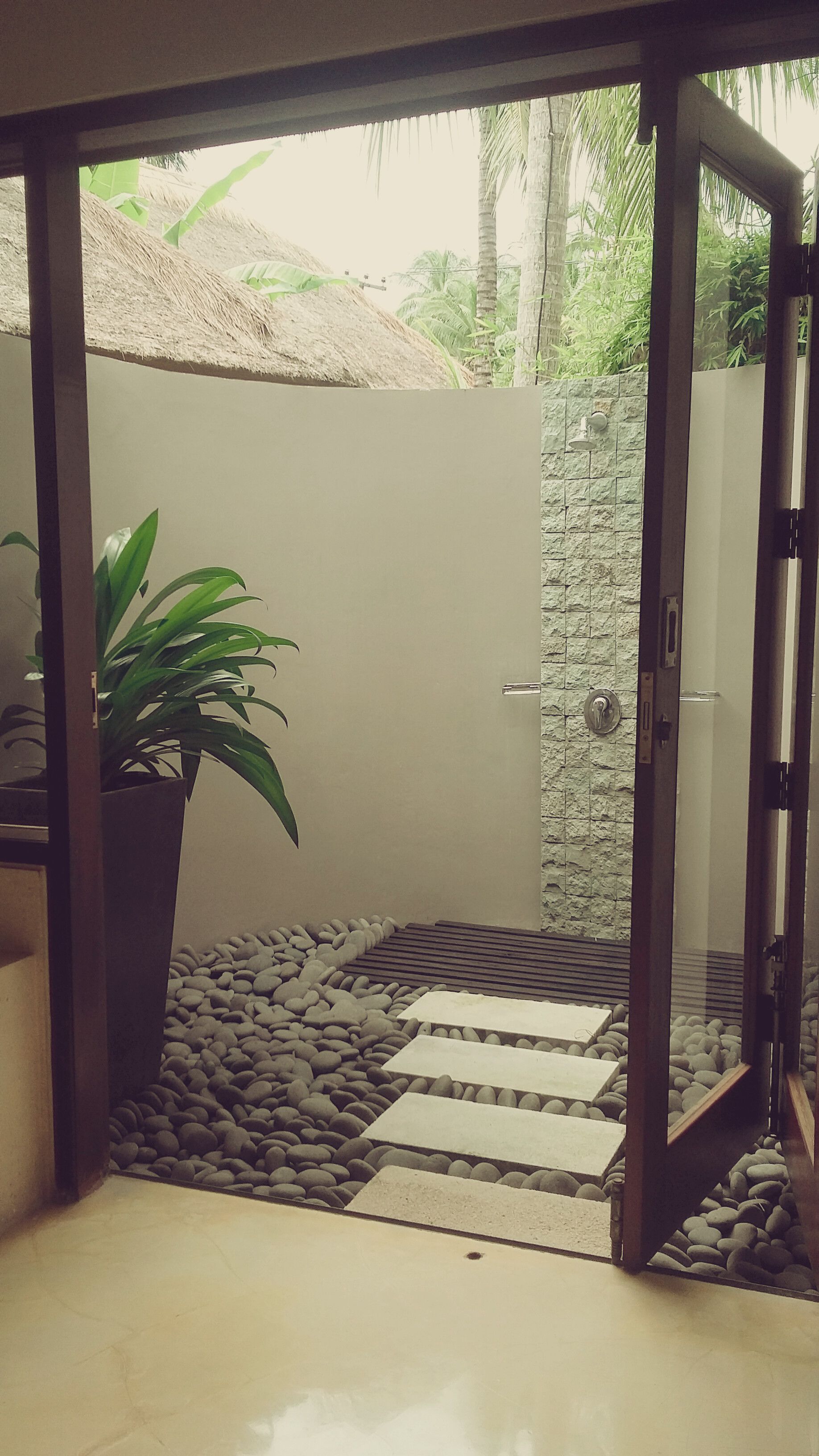 A glass-enclosed outdoor area with a stone wall, a potted plant, and a pathway.