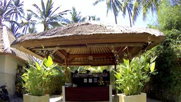 A thatched-roof structure with a counter and plants in front.