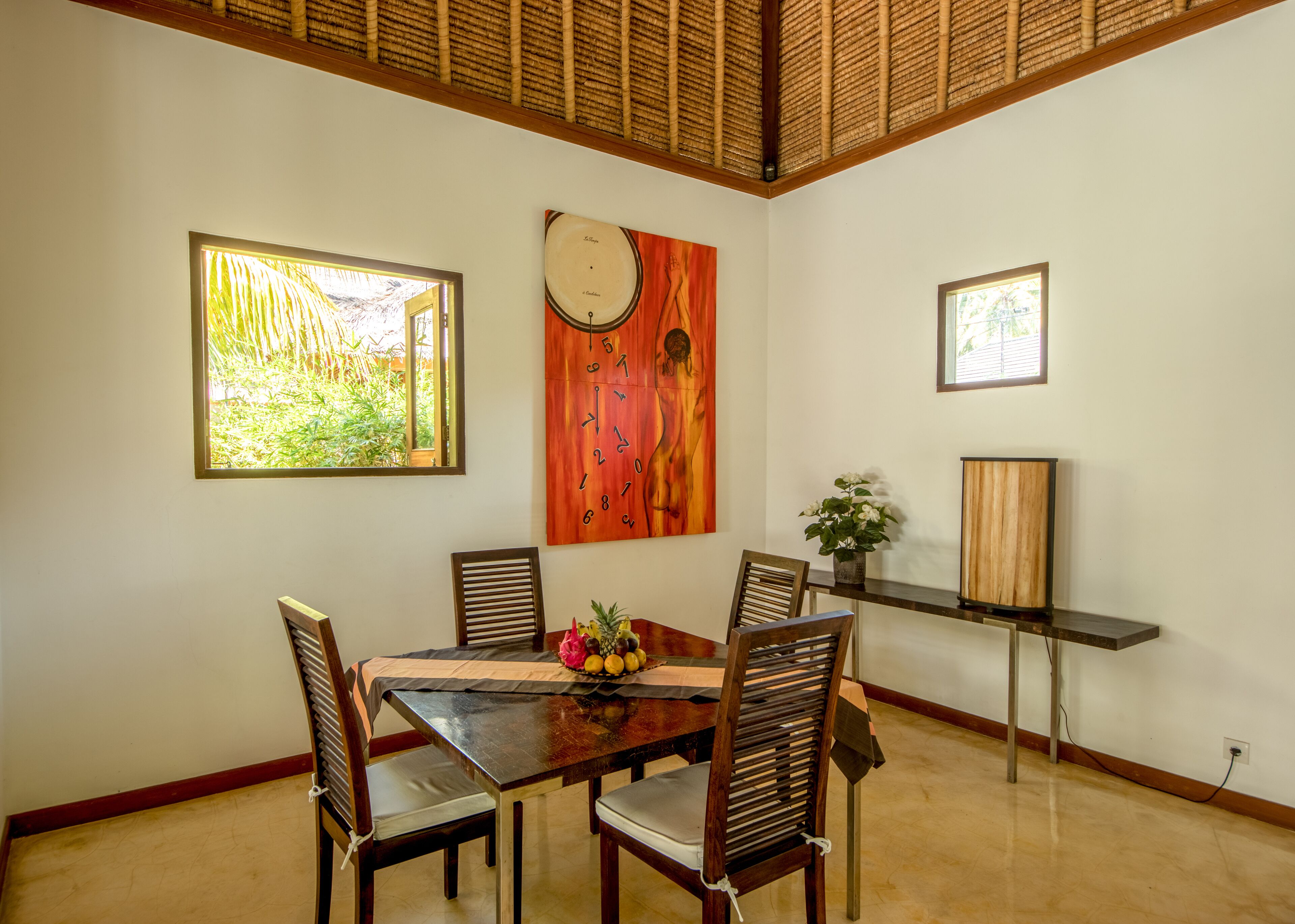 Un comedor con una mesa y sillas de madera, un reloj y una ventana con vistas a zonas verdes.