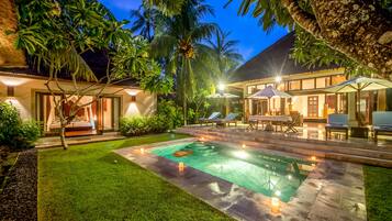 A well-lit outdoor pool area with lounge chairs and a thatched-roof structure.