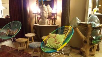 A room with two colorful woven chairs, a small stool, a wooden sculpture, and a Buddha statue.