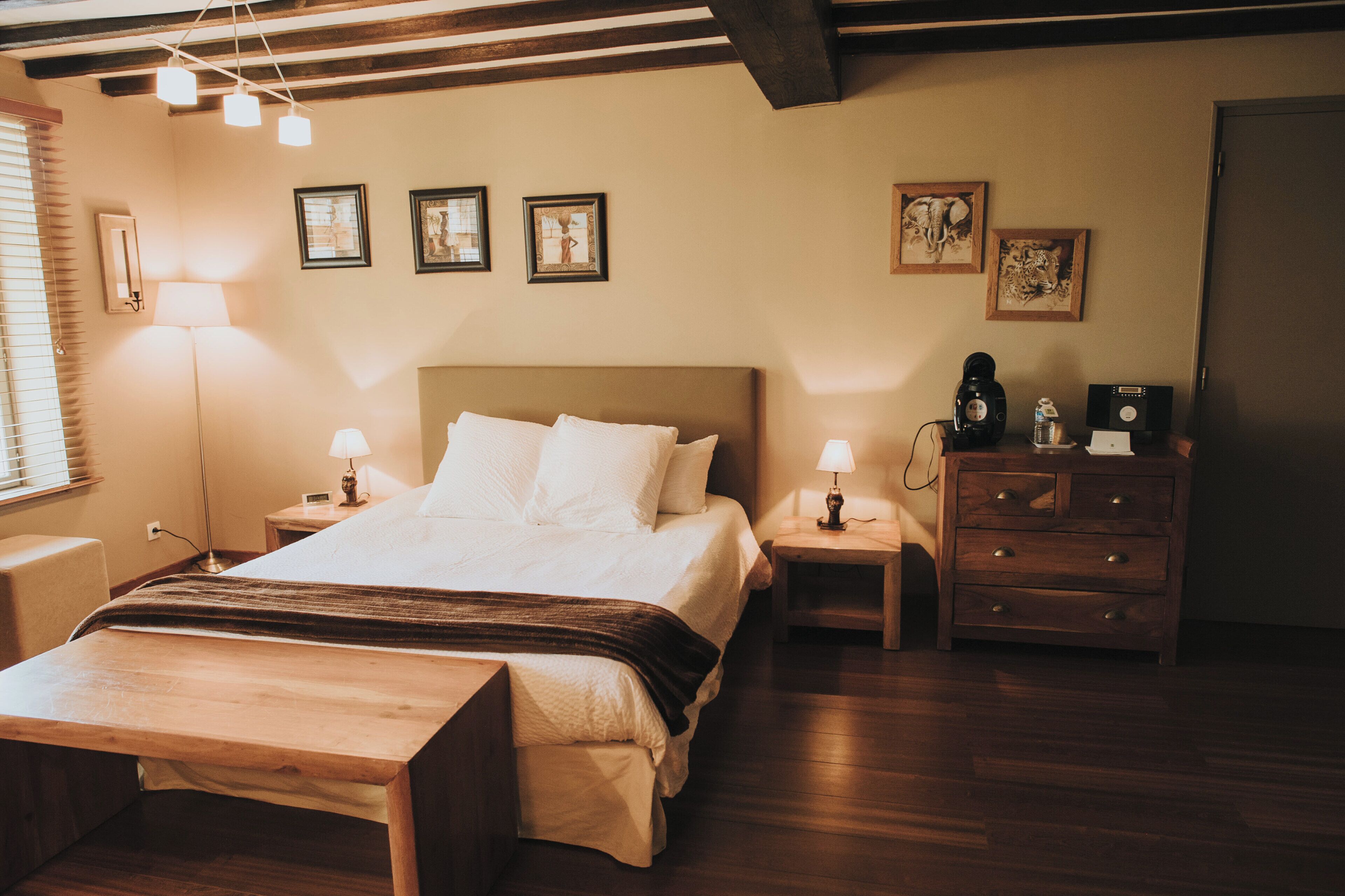 Une chambre à coucher bien rangée, avec un grand lit, des tables de chevet, une commode en bois et des œuvres d’art encadrées accrochées aux murs.