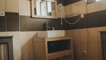 Un baño con tocador de madera, un lavamanos, un espejo, una lámpara colgante y un tapete estampado en el suelo.