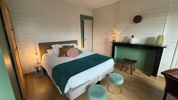 Une chambre à coucher avec un lit, une table de chevet, un mur vert, une cheminée et deux tabourets.