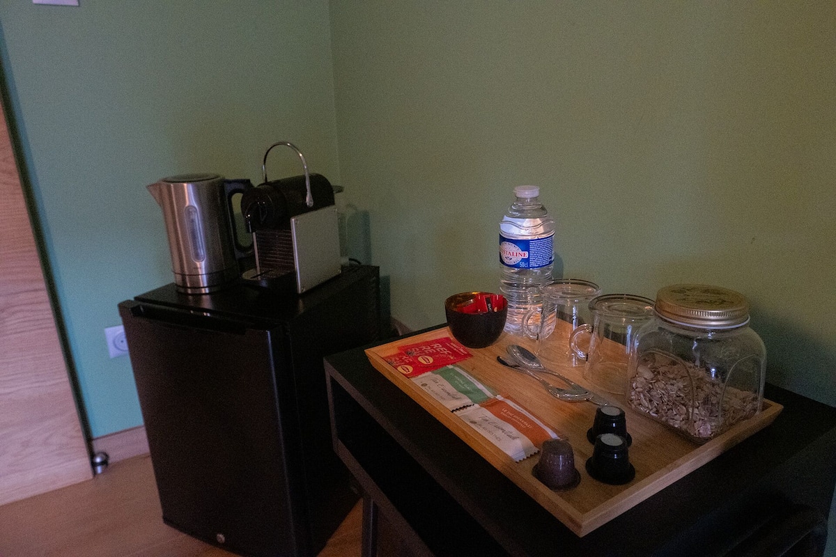 Een kitchenette met een koffiezetapparaat, een waterfles, potjes en toevoegingen op een houten dienblad.