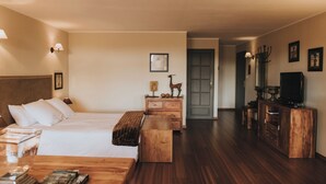A hotel room with a bed, wooden dresser, TV stand, and a hallway leading to a door. - Logis Hôtel-Restaurant Le Moulin D'Artres (Artres)