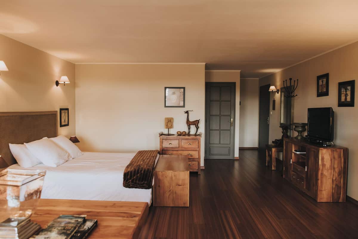 Een hotelkamer met een bed, een houten dressoir, een tv-meubel en een gang naar een deur.
