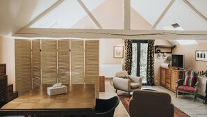 A spacious loft with a high ceiling, a wooden dining table, a comfortable sofa, and a television. - Logis Hôtel-Restaurant Le Moulin D'Artres (Artres)
